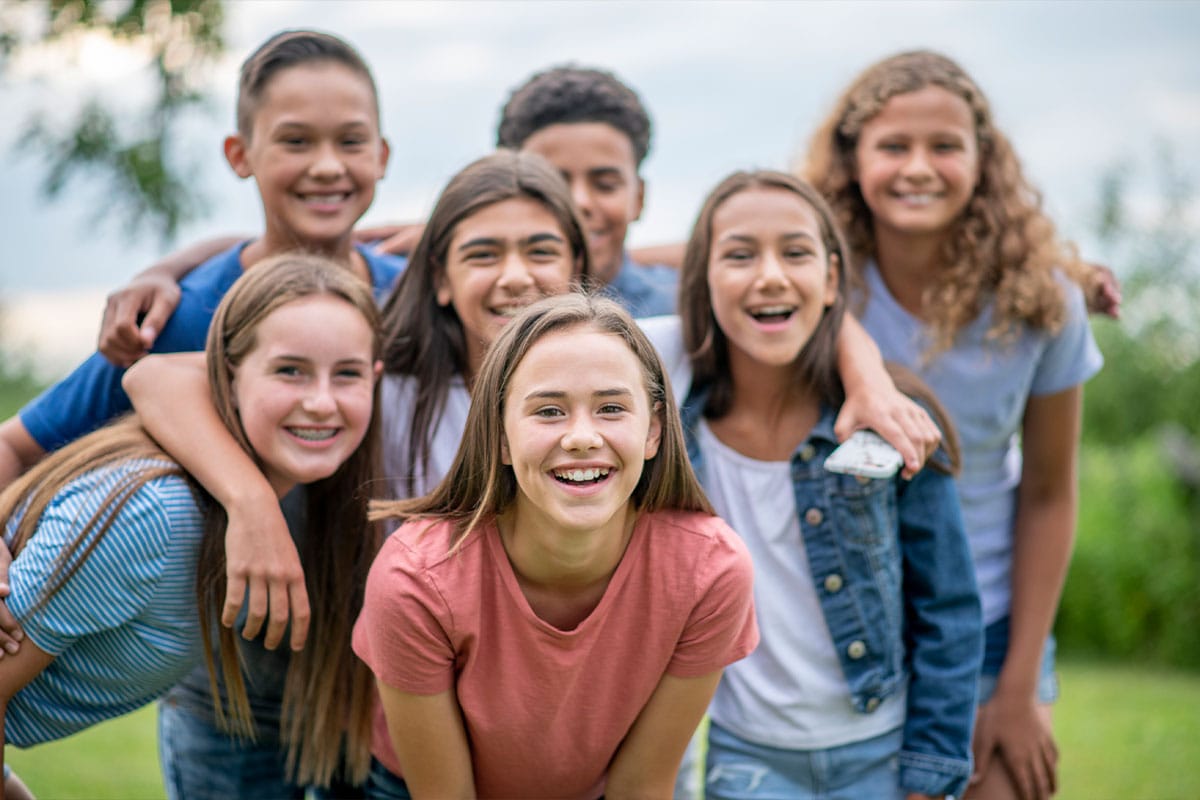 Group of smiling pre-teens and teenagers outdoors, with one girl in front showing straight teeth after Invisalign treatment in Encino